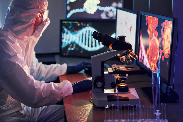 Monitors with information on the table. Scientist in white protective uniform works with coronavirus and blood tubes in laboratory. - Photo, image