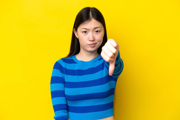 Young Chinese woman isolated on yellow background showing thumb down with negative expression - Fotoğraf, Görsel