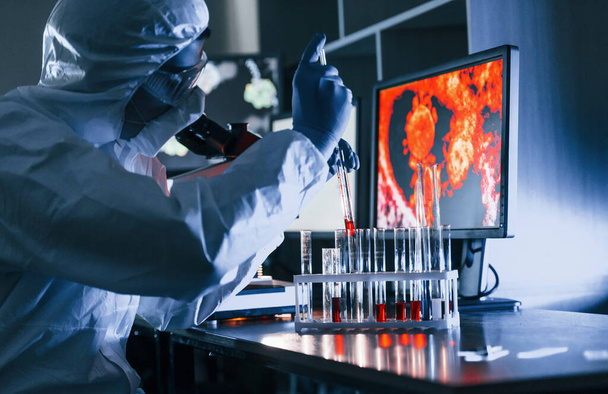 Beyaz koruyucu üniformalı bilim adamları laboratuarda koronavirüs ve kan tüpleriyle çalışıyorlar.. - Fotoğraf, Görsel