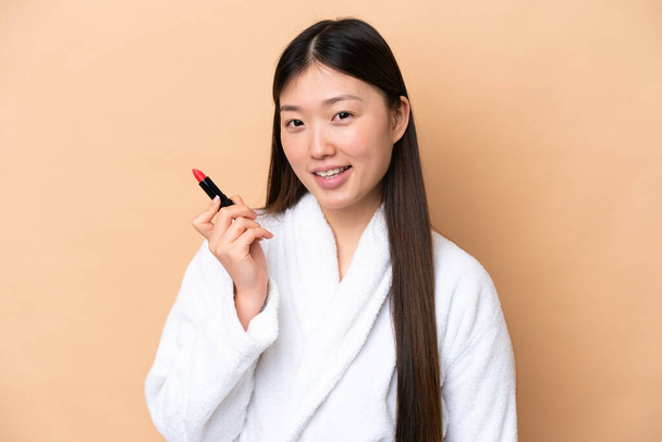 Young Chinese woman isolated on beige background holding red lipstick - Valokuva, kuva
