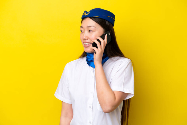 Avion hôtesse de l'air femme chinoise isolé sur fond jaune en gardant une conversation avec le téléphone portable avec quelqu'un - Photo, image