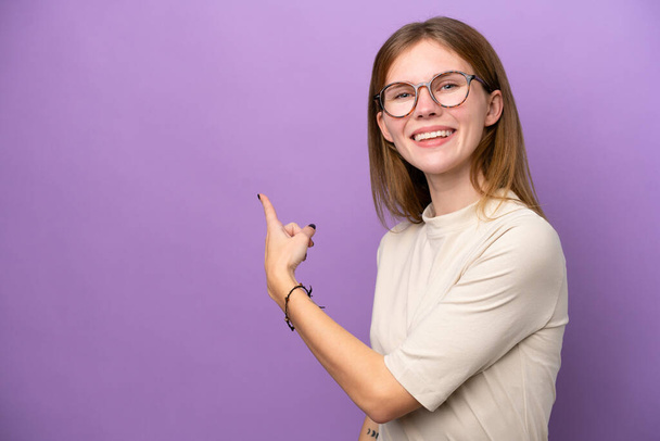 Young English woman isolated on purple background pointing back - 写真・画像