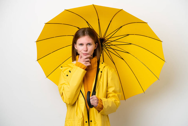 Young English woman with rainproof coat and umbrella isolated on white background thinking - Foto, Imagem