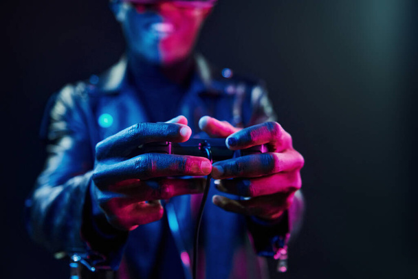 Virtual reality experience. Futuristic neon lighting. Young african american man in the studio. - 写真・画像