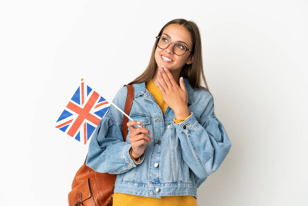 Young hispanic woman holding an United Kingdom flag over isolated white background looking up while smiling - Φωτογραφία, εικόνα
