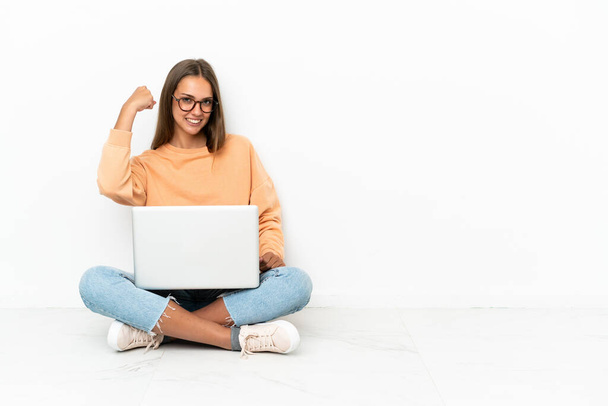 jonge vrouw met een laptop zitten op de vloer doen sterk gebaar - Foto, afbeelding