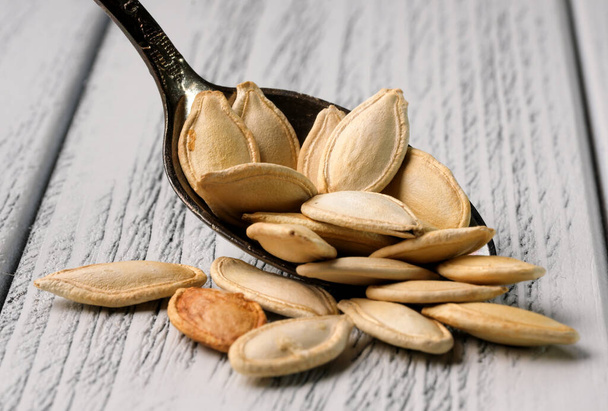 Roasted unpeeled pumpkin seeds in a teaspoon on a wooden light table close-up - Foto, immagini