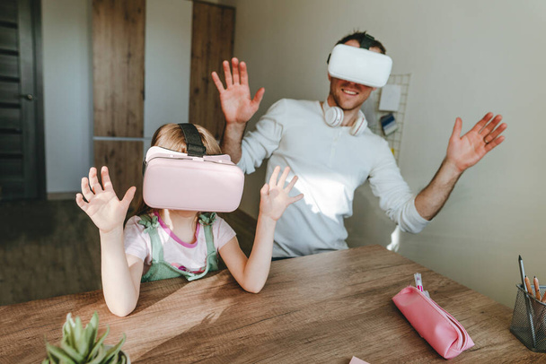 5 jaar oud meisje met plezier tijd met haar vader met behulp van VR bril thuis voor gaming of leren. Familie activiteiten concept. Moderne technologie gebruikt door familie. Selectieve focus. - Foto, afbeelding