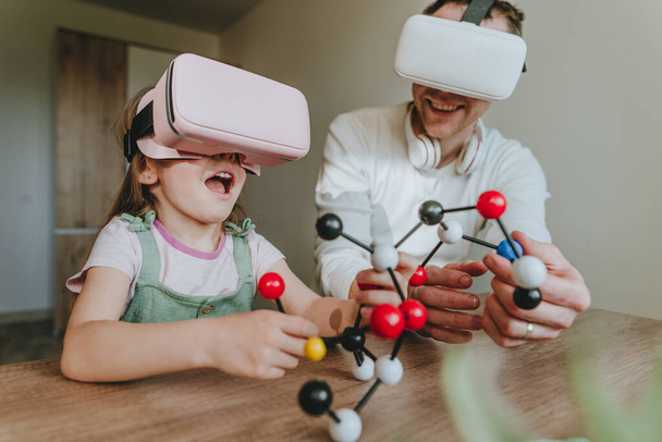 Little girl having fun time with her father using VR glasses at home for learning molecular structure. Homeschooling concept. Modern technology using by family. Selective focus. - Fotó, kép
