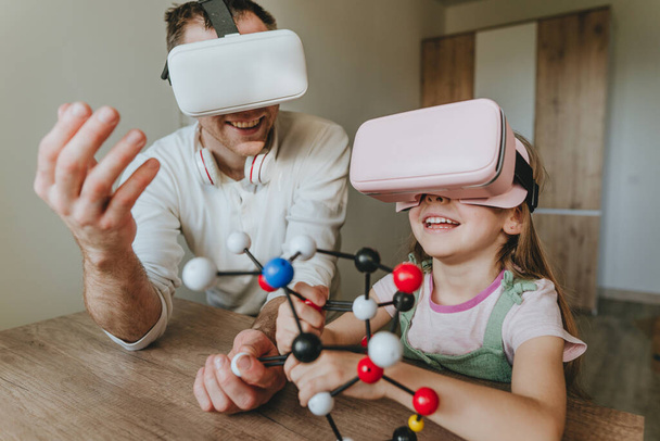 Pikkutyttö pitää hauskaa isänsä kanssa käyttäen VR-laseja kotona molekyylirakenteen oppimiseen. Kotikoulun konsepti. Modernia teknologiaa käyttäen perheen. Valikoiva painopiste. - Valokuva, kuva