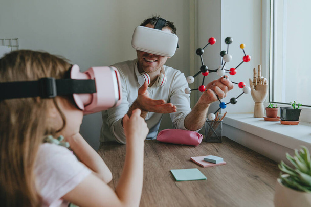 Young man describing his daughter configuration of a molecule using VR glasses. Modern technology using by family. Homeschooling concept. Selective focus. - Foto, imagen