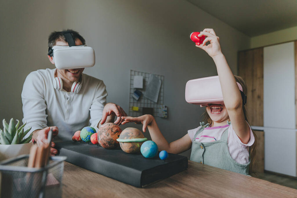 Little girl having fun time with her father using VR glasses at home for learning Solar system planets. Homeschooling concept. Modern technology using by family. Selective focus. - Photo, image