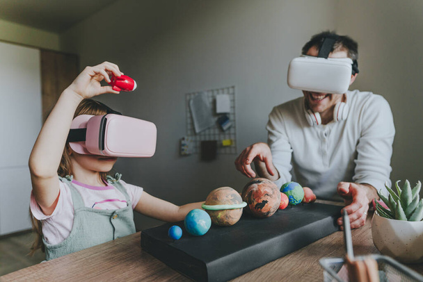 La bambina si diverte con suo padre usando occhiali VR a casa per imparare i pianeti del sistema solare. Concetto di istruzione a casa. Tecnologia moderna che utilizza dalla famiglia. Focus selettivo. - Foto, immagini
