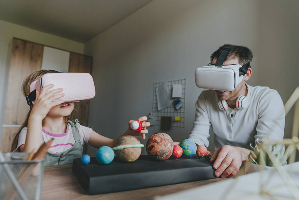 Küçük kız evde güneş sistemi gezegenlerini öğrenmek için VR gözlüğü kullanarak babasıyla eğleniyor. Evde eğitim kavramı. Aile tarafından kullanılan modern teknoloji. Seçici odak. - Fotoğraf, Görsel