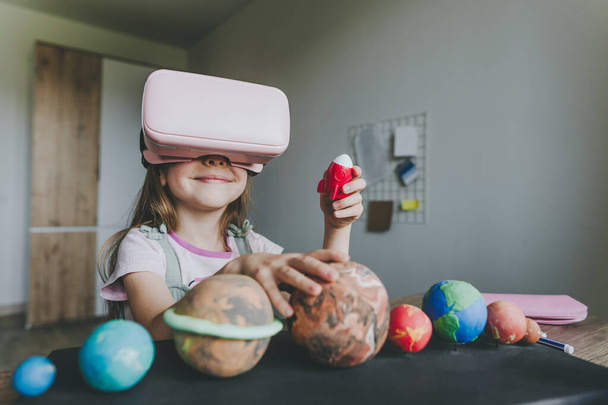 Klein meisje met VR bril thuis voor het leren van Zonnestelsel planeten. Modern onderwijswetenschappelijk concept. Selectieve focus. - Foto, afbeelding
