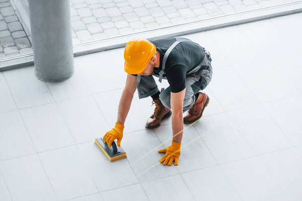 Top view of man in grey uniform that installing plate indoors in modern big office at daytime. - Foto, afbeelding