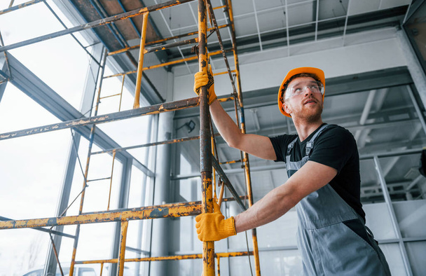 Man in grey uniform works with construction indoors in modern big office at daytime. - Φωτογραφία, εικόνα