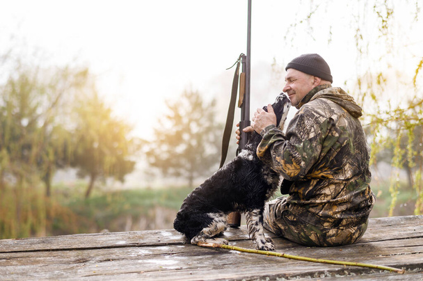 Male hunter sits on a bridge with a Russian spaniel  - Foto, imagen