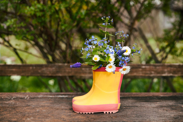 Yellow rubber boots with spring flowers bouquet on rough rural wooden background. Natural background, rustic seasonal composition. Copy space for text. - Fotoğraf, Görsel