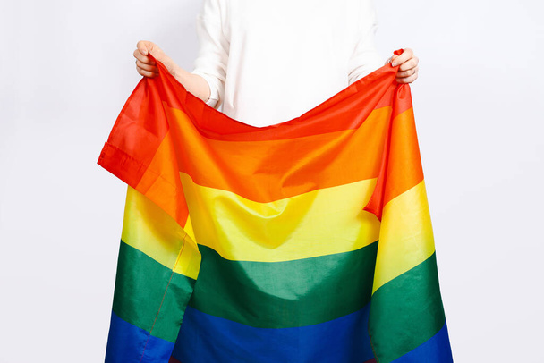 Bandera de orgullo, bandera LGBTQ, bandera arco iris en manos femeninas sobre fondo blanco - Foto, imagen