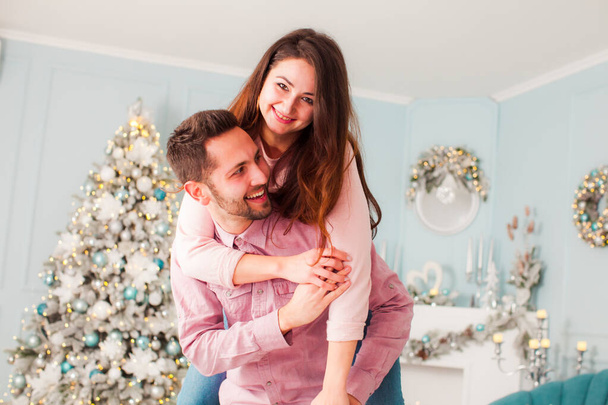 Young happy couple have fun and huggingnear christmas tree - Фото, изображение