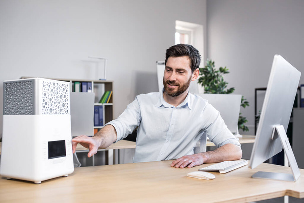 Happy businessman works in office hot, turns on portable small air conditioner freshener and humidifier - Fotografie, Obrázek