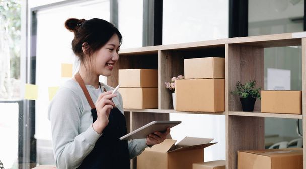 Young beautiful happy asian business woman owner of SME online using laptop receive order from customer with parcel box packaging at her startup home office, online business seller and deliver - Photo, Image