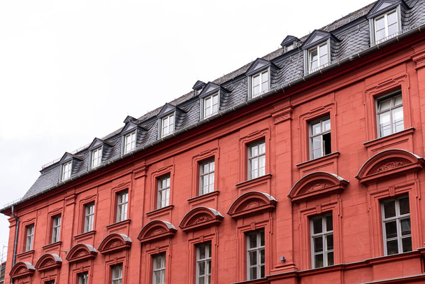 Vibrant red stone tenement or apartment building with shiny black roof tiles, attic windows (dormers), many windows with geometric ornament and triangle pediments. - Fotoğraf, Görsel