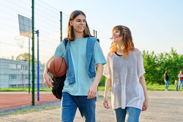 Young teenage male female students with ball walking outdoor near basketball court - Фото, зображення