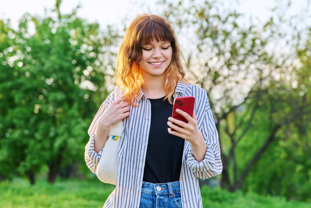 Outdoor portrait of trendy young red-haired girl with smartphone in hand - Фото, зображення