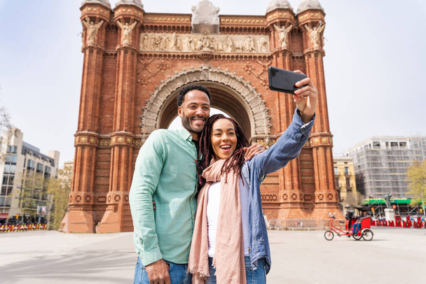 Beautiful happy hispanic latino couple of lovers dating outdoors - Tourists in Barcelona having fun during summer vacation and visiting Arc de Triumf historic landmark - Foto, afbeelding