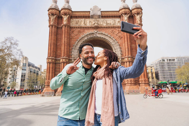 Beautiful happy hispanic latino couple of lovers dating outdoors - Tourists in Barcelona having fun during summer vacation and visiting Arc de Triumf historic landmark - Photo, image