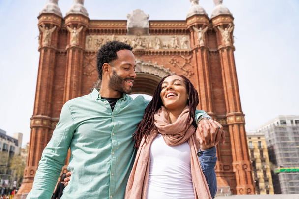 Beautiful happy hispanic latino couple of lovers dating outdoors - Tourists in Barcelona having fun during summer vacation and visiting Arc de Triumf historic landmark - Photo, image