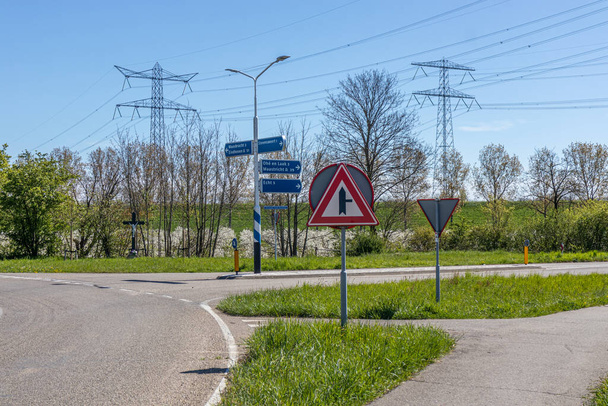 Country road with a caution triangle next crossroads and signs indicating the direction to Echt, Maastricht, Ohe en Laak, Maasbracht and Eindhoven in Stevensweert, South Limburg, Netherlands - Foto, imagen