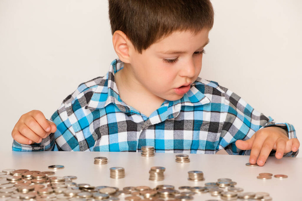A preschool boy in a plaid shirt counts coins, builds towers. Financial literacy for children. - Zdjęcie, obraz