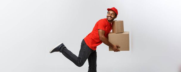 Concepto de entrega: el guapo repartidor afroamericano corre corriendo para entregar un paquete para el cliente. Aislado en Grey studio Background. Copiar espacio
. - Foto, imagen