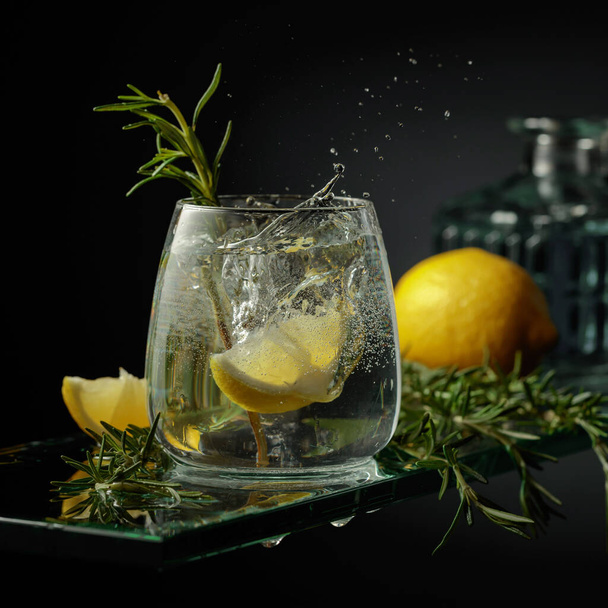 Cocktail tonico al gin con limone e rosmarino. La fetta di limone cade in vetro con un cocktail. - Foto, immagini
