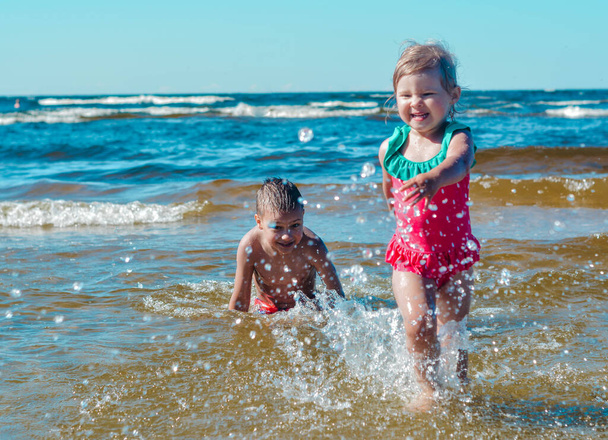 Fille et garçon d'apparence européenne s'amuser dans l'eau sur la plage et éclaboussures - Photo, image