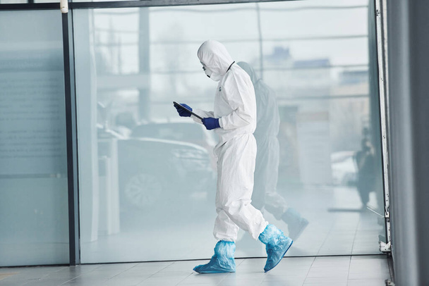 Male doctor scientist in lab coat, defensive eyewear and mask holding notepad in hands. - 写真・画像