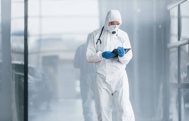 Male doctor scientist in lab coat, defensive eyewear and mask holding notepad in hands. - Fotó, kép