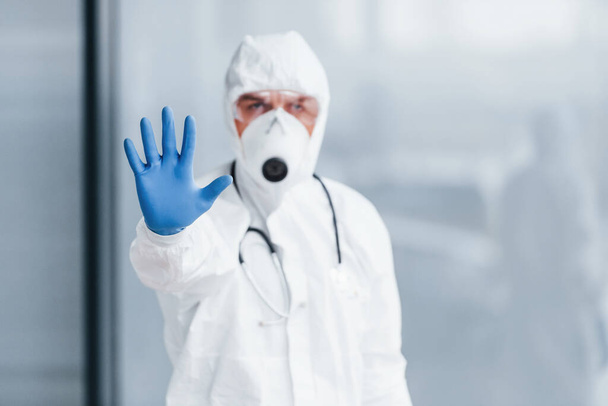 Shows stop gesture by hand. Male doctor scientist in lab coat, defensive eyewear and mask. - Fotó, kép
