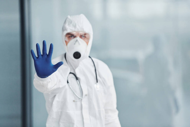 Shows stop gesture by hand. Male doctor scientist in lab coat, defensive eyewear and mask. - Fotó, kép