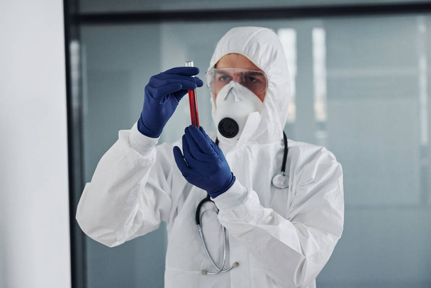 Hombre científico médico en bata de laboratorio, gafas defensivas y máscara sostiene tubo de ensayo con sangre. - Foto, Imagen