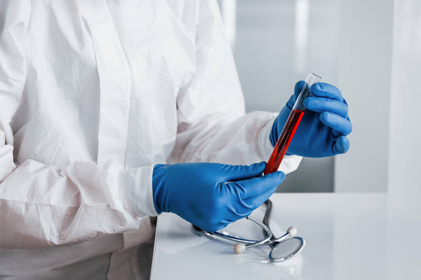 Male doctor scientist in lab coat, defensive eyewear and mask holds test tube with blood. - Photo, image