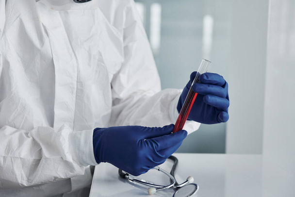 Male doctor scientist in lab coat, defensive eyewear and mask holds test tube with blood. - Foto, Bild