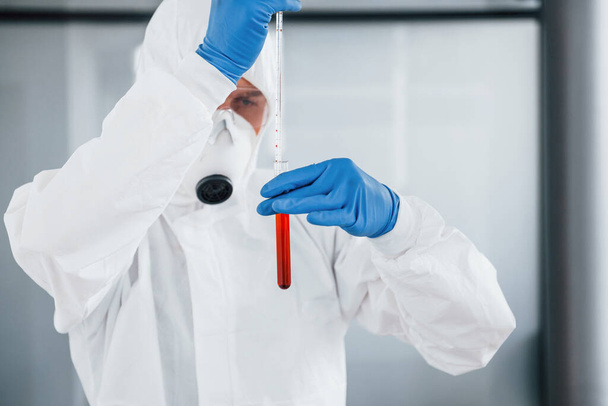 Male doctor scientist in lab coat, defensive eyewear and mask works with test tube with blood inside of it. - Foto, Bild