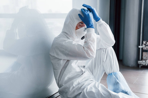 Tired doctor scientist in lab coat, defensive eyewear and mask sits and takes break. - Foto, Bild