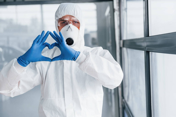 Male doctor scientist in lab coat, defensive eyewear and mask shows love gesture by hands. - Фото, зображення