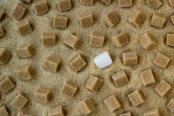 Cubos naturales de azúcar morena diseñados sobre azúcar morena granulada, fondo - Foto, Imagen