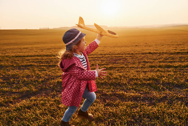Cute little girl runs with toy plane on the beautiful field at sunny daytime. - Фото, зображення